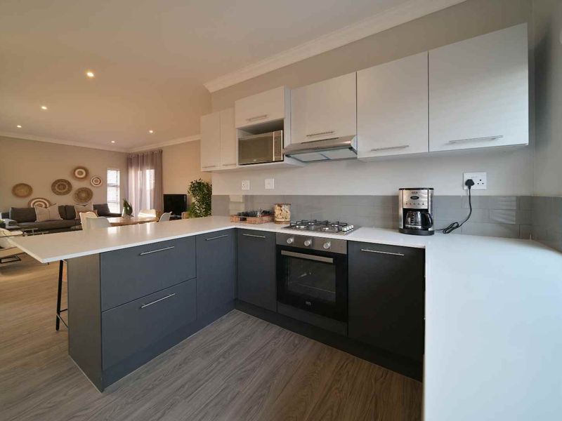 Modern open-plan kitchen featuring sleek two-tone cabinetry, quartz countertops, integrated appliances, and high-quality laminate flooring, flowing seamlessly into the adjacent living area.