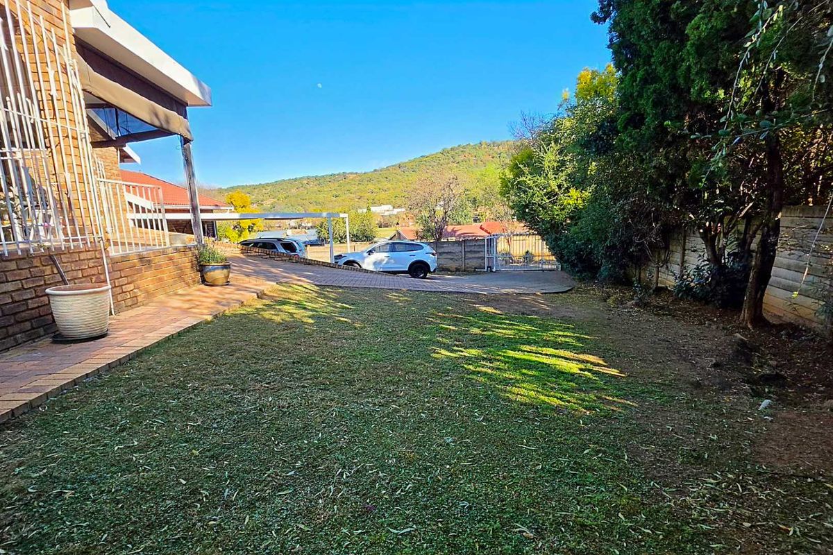A view of the rear garden area featuring a paved walkway, established trees, and a boundary wall with mountain views in the background.