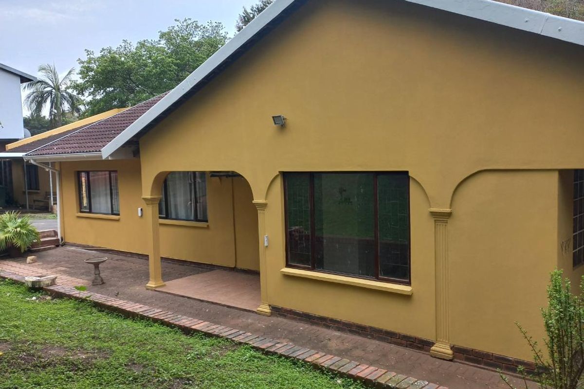 Rear view of the house featuring a covered patio area, brick paving, and decorative columns, set against a garden space.
