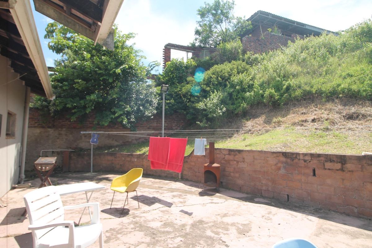 A rear outdoor patio area featuring a brick retaining wall, concrete paving, and a clothesline, set against a sloped garden backdrop.
