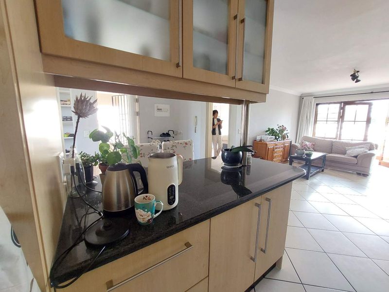 Open plan kitchen and living area featuring granite countertops, light wood cabinetry with frosted glass inserts, and neutral tiled flooring throughout.