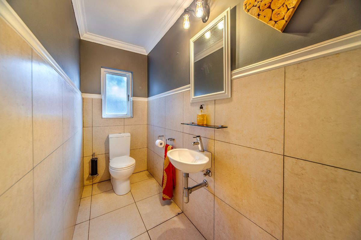 A modern guest bathroom featuring neutral floor-to-ceiling tiling, a wall-mounted basin with chrome fixtures, and a clean, contemporary aesthetic.