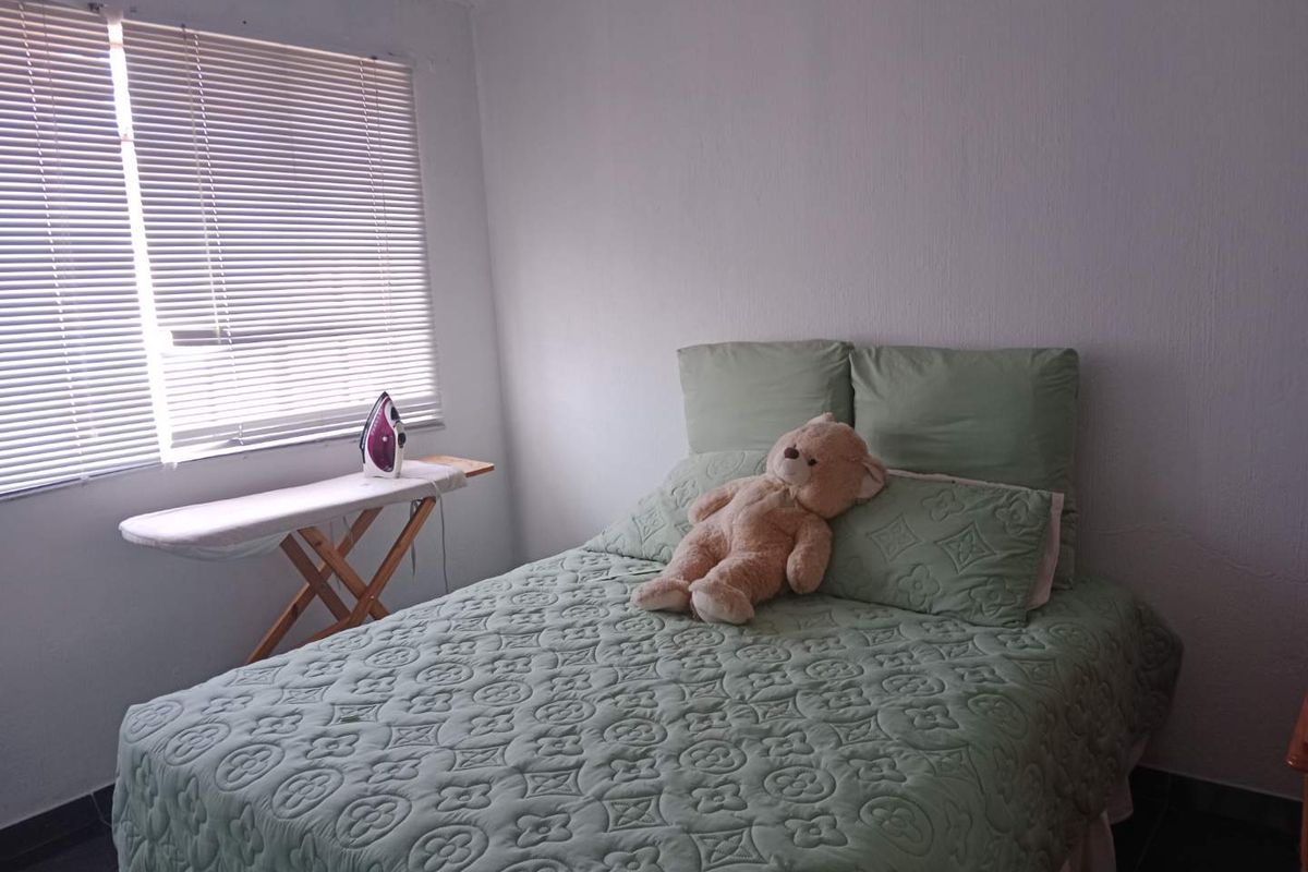 A simple bedroom featuring tiled flooring, white walls, and venetian blinds, providing a functional and neutral space.