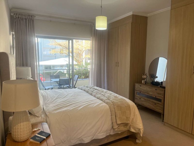 A well-maintained bedroom featuring built-in wooden cupboards, carpeted flooring, and a sliding glass door providing access to a private balcony.