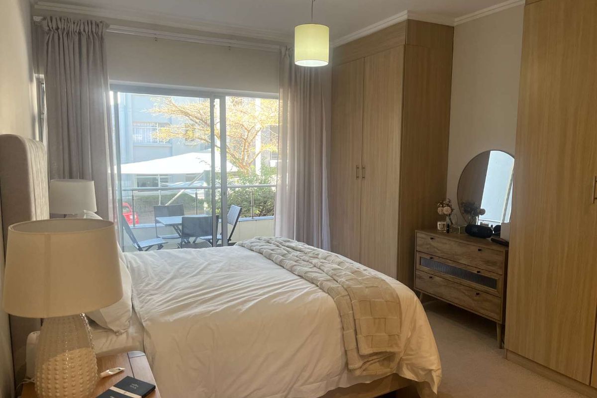 A well-maintained bedroom featuring built-in wooden cupboards, carpeted flooring, and a sliding glass door providing access to a private balcony.