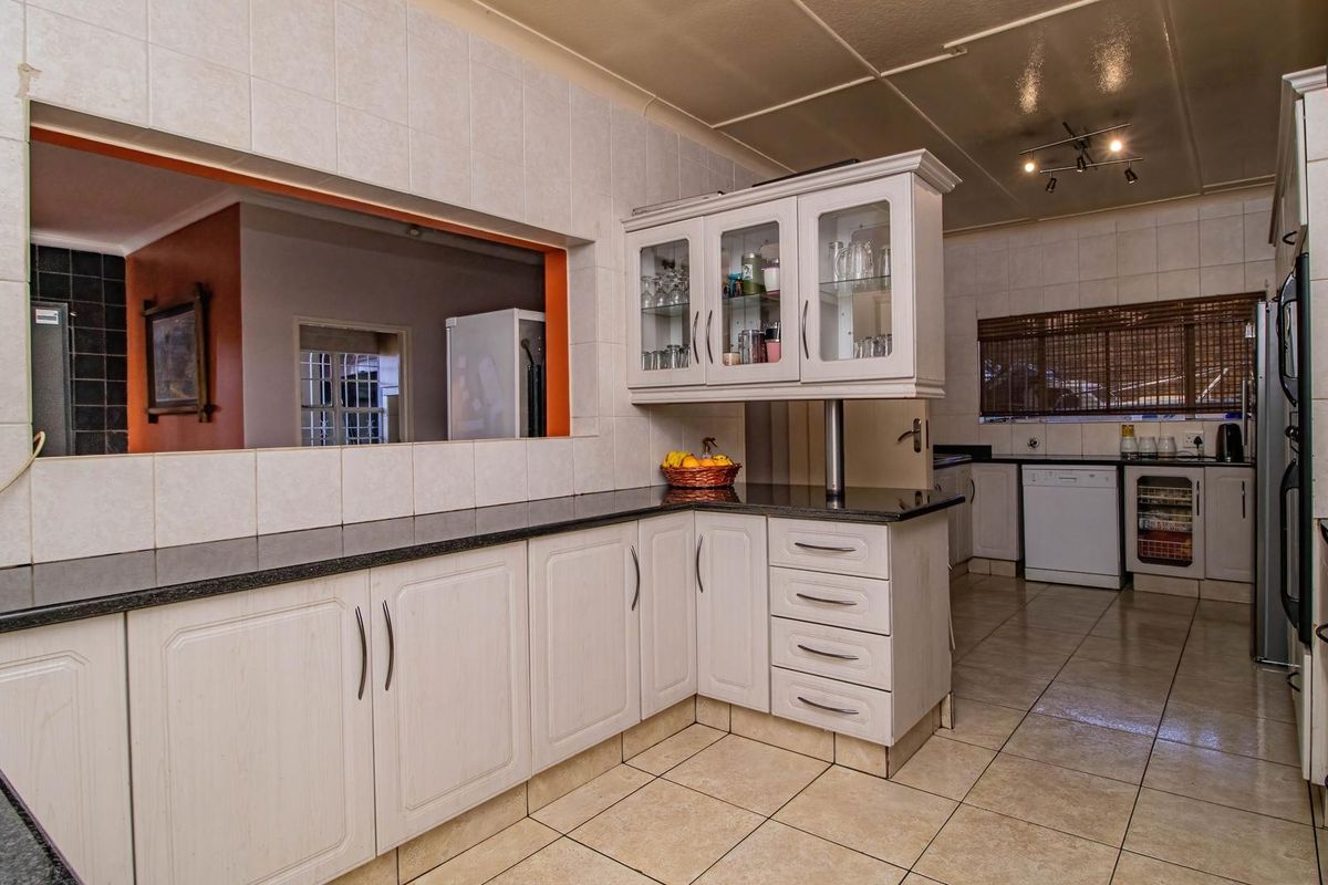 A functional kitchen featuring light-toned cabinetry, dark granite countertops, tiled flooring, and a convenient serving hatch opening into the adjacent living area.