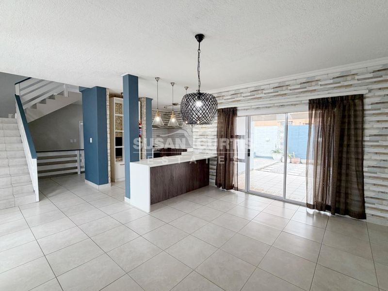 Spacious open-plan living area featuring a modern kitchen island, stone veneer accents, tiled flooring, and direct access to the rear patio through sliding doors.