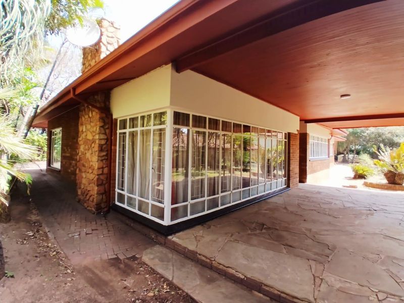 A covered patio area featuring flagstone paving, a timber ceiling, and stone-clad exterior walls with large steel-framed windows.
