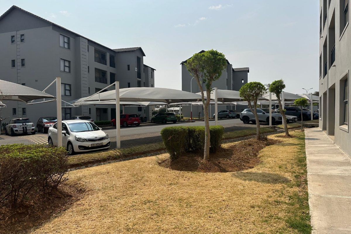 Exterior view of the apartment complex featuring paved parking areas with shade cloth carports and landscaped garden beds.