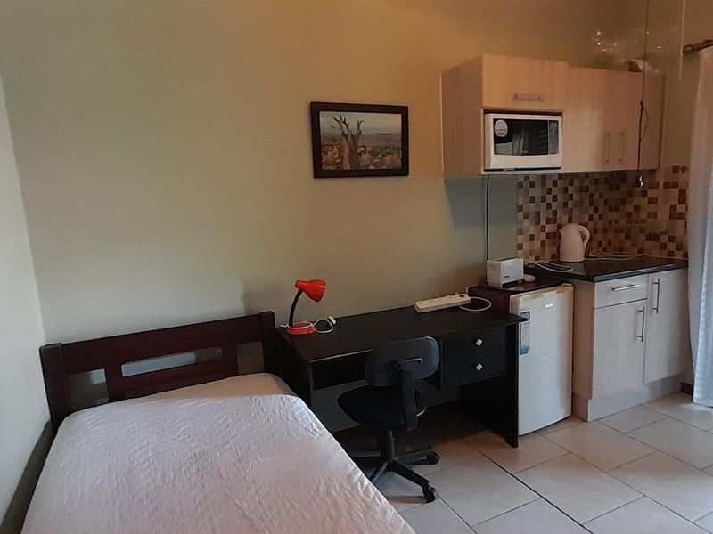 Compact open-plan studio apartment featuring a kitchenette with built-in cabinetry, tiled flooring, and direct access to an outdoor area via sliding doors.