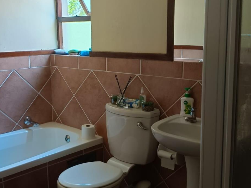 A functional bathroom featuring a bathtub, pedestal basin, and toilet with diamond-patterned wall tiling.