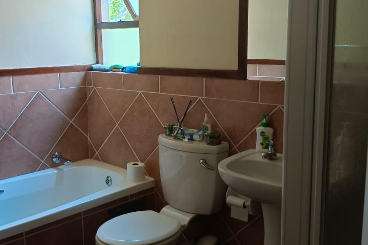 A functional bathroom featuring a bathtub, pedestal basin, and toilet with diamond-patterned wall tiling.