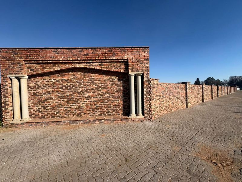 A well-maintained face brick boundary wall featuring decorative stone columns, bordering a paved driveway on a residential property.