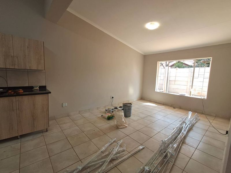 An open-plan living and kitchen area featuring tiled flooring, built-in cabinetry with granite countertops, and natural light from a large window.