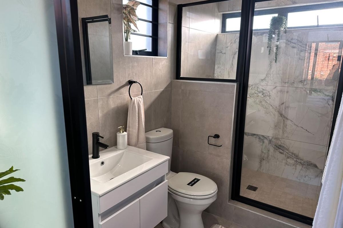 Modern bathroom featuring a vanity with basin, black fixtures, and a spacious walk-in shower with marble-look wall tiles and black frame detailing.