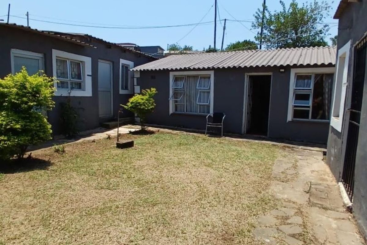 Rear exterior view of the townhouse featuring a small lawn area, stone paved pathway, and corrugated metal roofing.