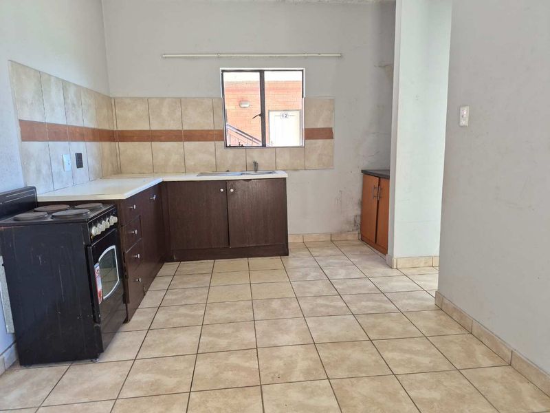 A functional kitchen featuring dark wood cabinetry, tiled backsplash, and tiled flooring, currently vacant and ready for renovation or modernization.