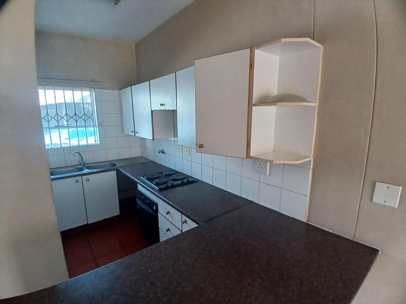 A functional kitchen featuring built-in cabinetry, laminate countertops, an electric hob, and an oven, with tiled splashbacks and security bars on the window.
