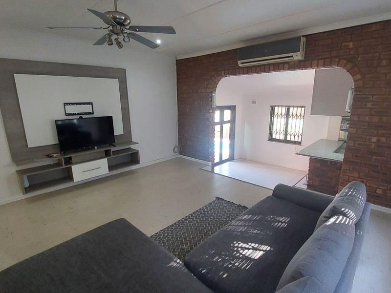 Open-plan living area featuring an exposed brick feature wall, built-in media cabinetry, ceiling fan, and split-system air conditioning unit.