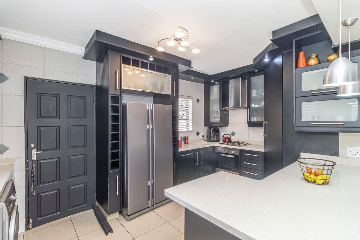 Modern kitchen featuring dark cabinetry, stone countertops, built-in oven, gas hob, extractor fan, and tiled flooring.