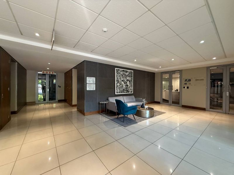 Modern office building entrance lobby featuring polished tiled flooring, a suspended ceiling with recessed lighting, and secure glass access doors.