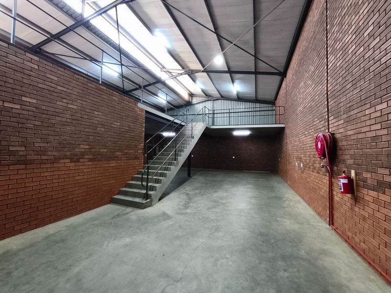 Spacious industrial utility area featuring exposed brick walls, concrete flooring, a mezzanine level with metal staircase, and integrated fire safety equipment.