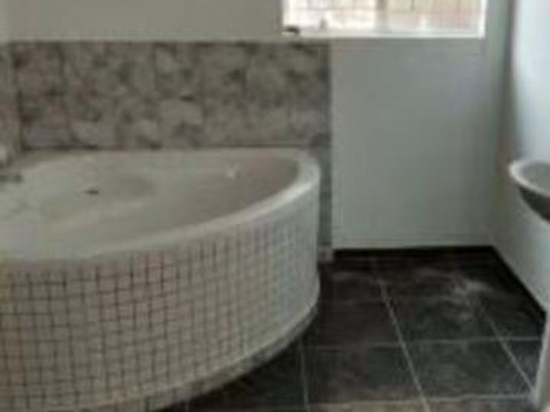 A bathroom featuring a corner bathtub with tiled surround and dark floor tiles, illuminated by a window with security bars.
