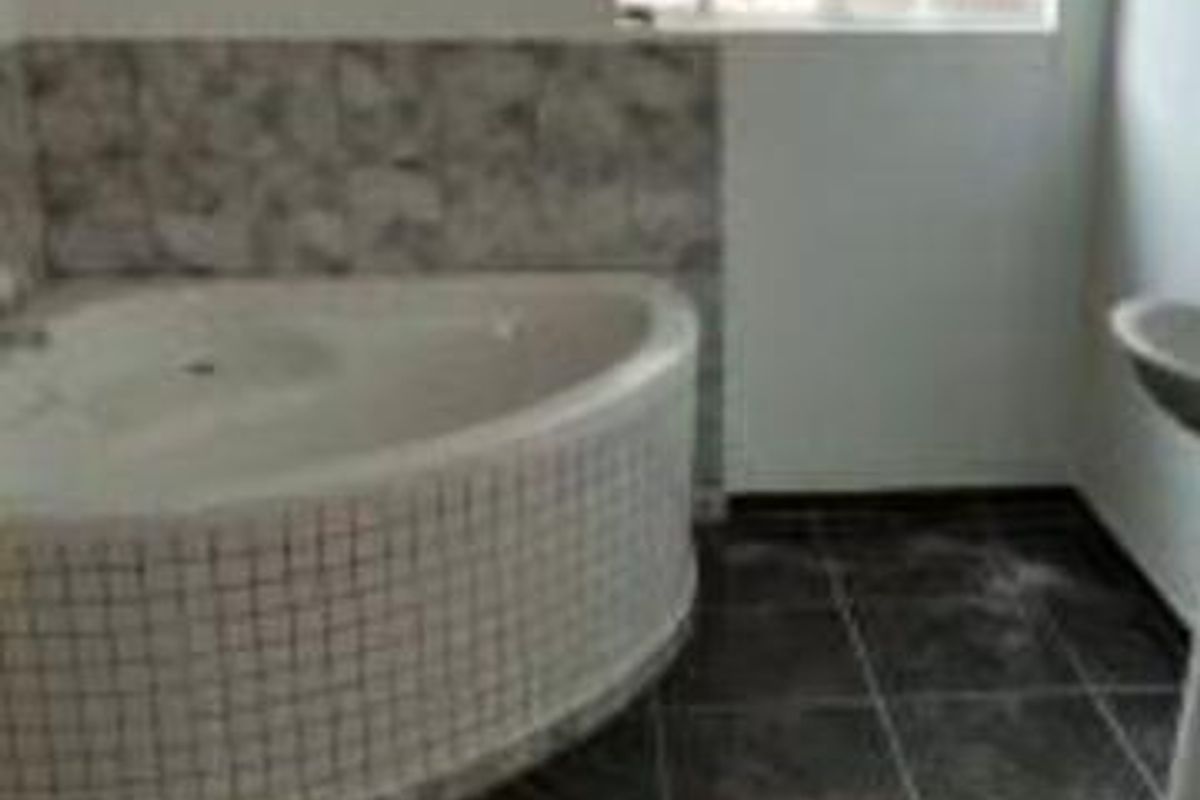 A bathroom featuring a corner bathtub with tiled surround and dark floor tiles, illuminated by a window with security bars.
