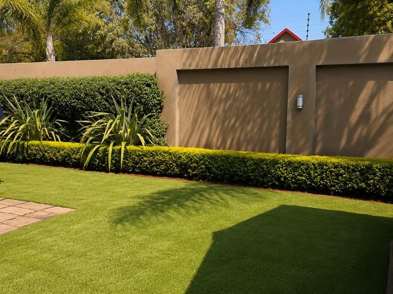 A well-maintained private garden featuring a manicured lawn, neat hedging, paved sections, and a secure boundary wall with integrated lighting and electric fencing.