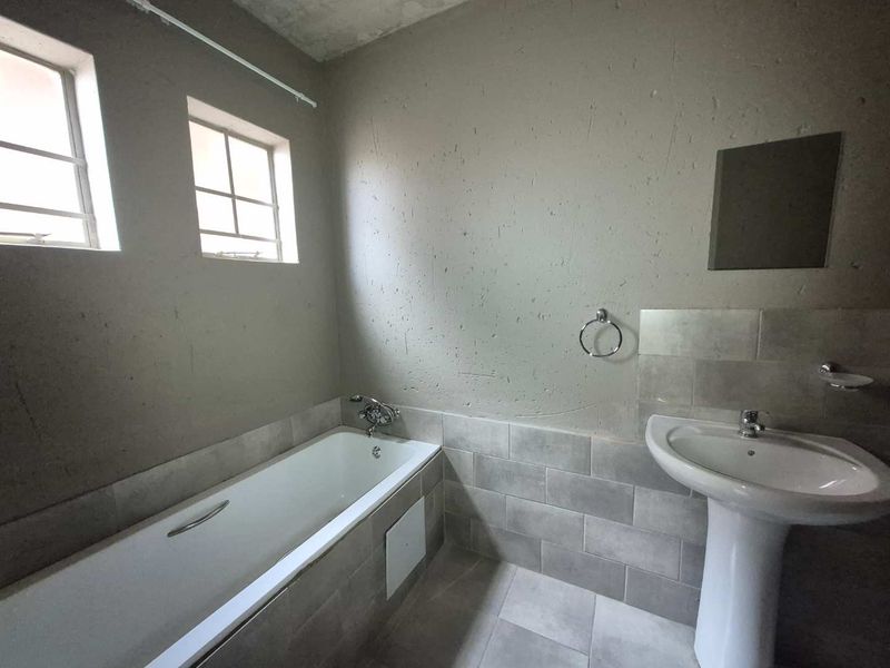 A basic bathroom featuring a bathtub, pedestal basin, and tiled finishes, currently requiring cosmetic updates to the wall surfaces and ceiling.