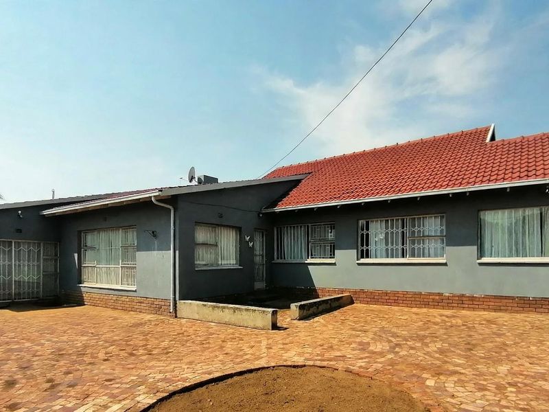 Rear exterior view of the house featuring a large brick-paved patio area, tiled roof, and security bars on the windows.