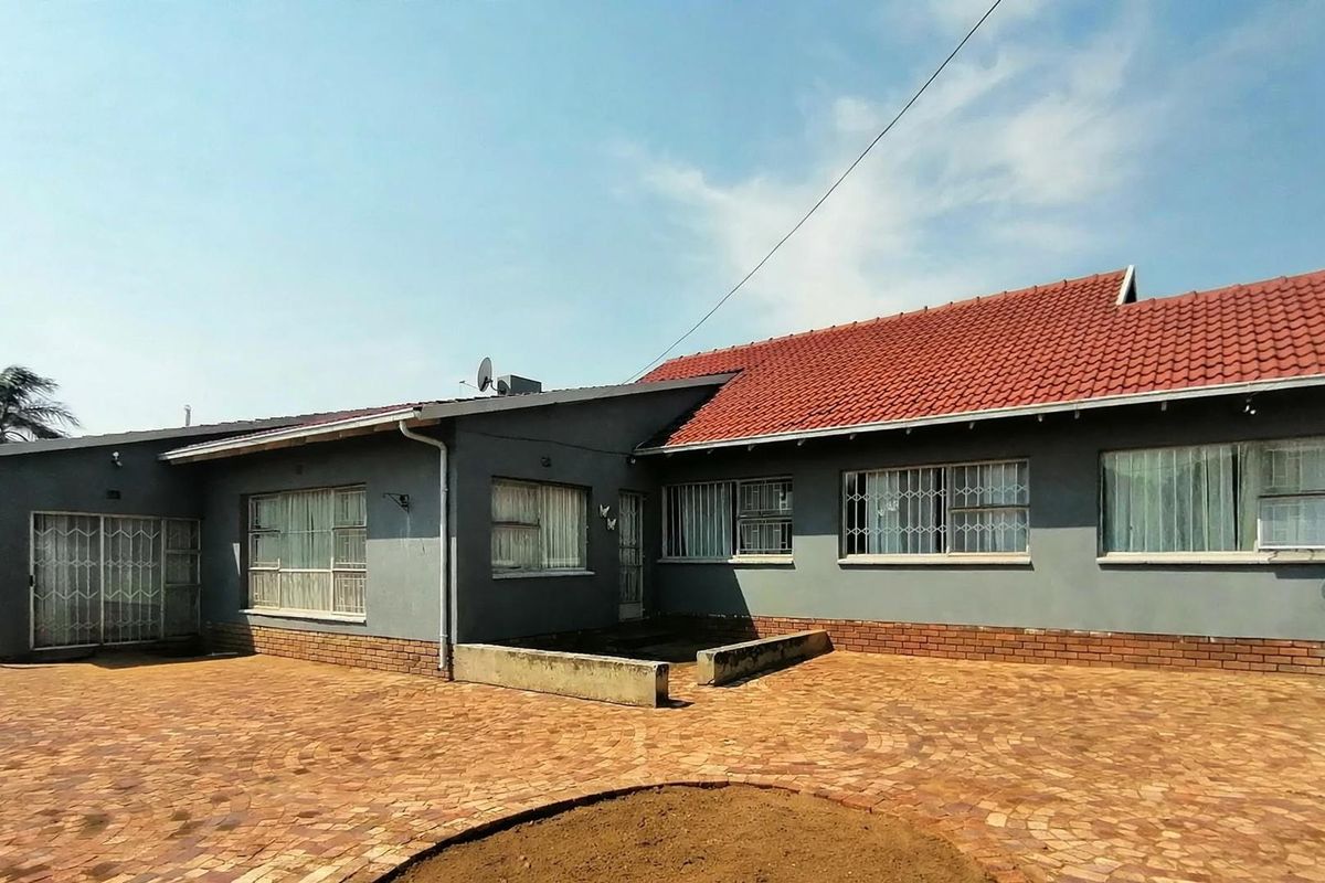 Rear exterior view of the house featuring a large brick-paved patio area, tiled roof, and security bars on the windows.