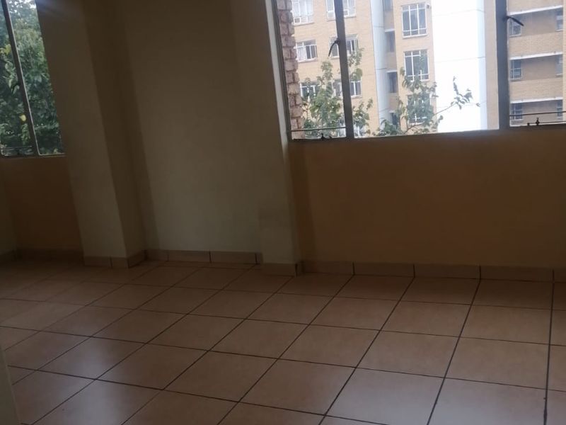 An empty living room featuring tiled flooring and large windows that provide natural light and an urban view.