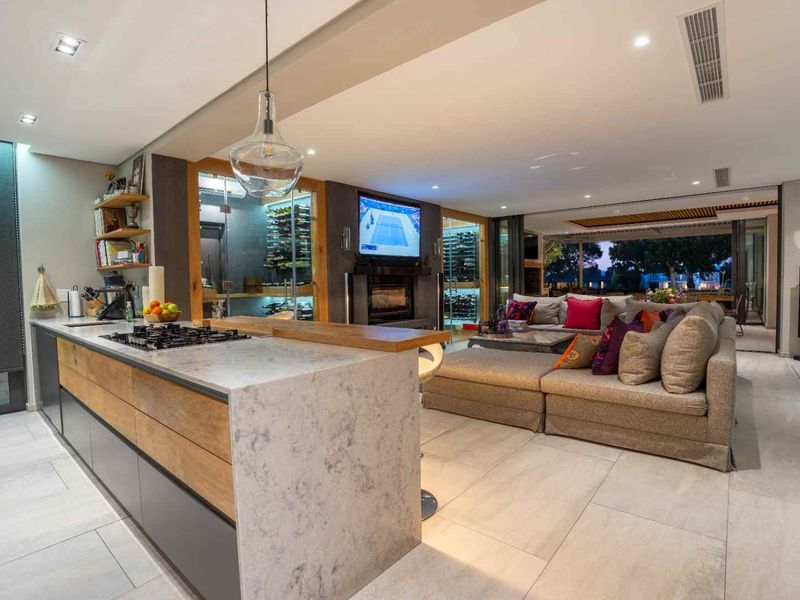 Modern open-plan living area featuring a sleek kitchen island with gas cooktop, stone countertops, integrated wine cellar, and seamless flow to the outdoor patio.