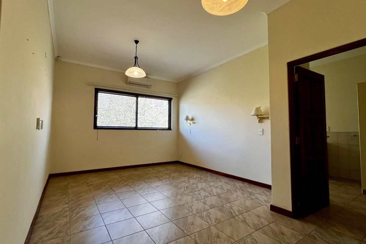 An empty bedroom featuring tiled flooring, a split-system air conditioner, and wall-mounted lighting, with an adjoining doorway leading to an ensuite area.
