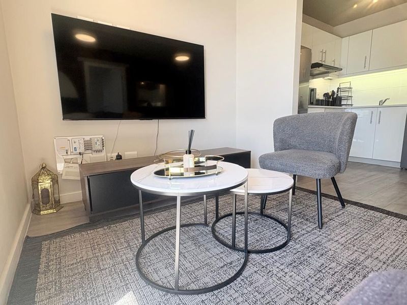 Open-plan living area featuring a modern kitchen with white cabinetry, integrated laundry appliances, and laminate flooring throughout.