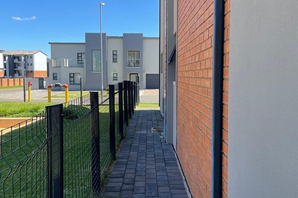 A side view of the townhouse exterior featuring a brick facade, paved walkway, and secure wire mesh fencing.