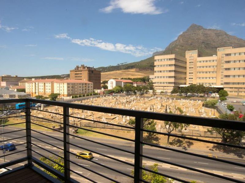 A balcony featuring a modern metal balustrade and decking, offering an elevated urban view of the surrounding neighbourhood and mountain landscape.