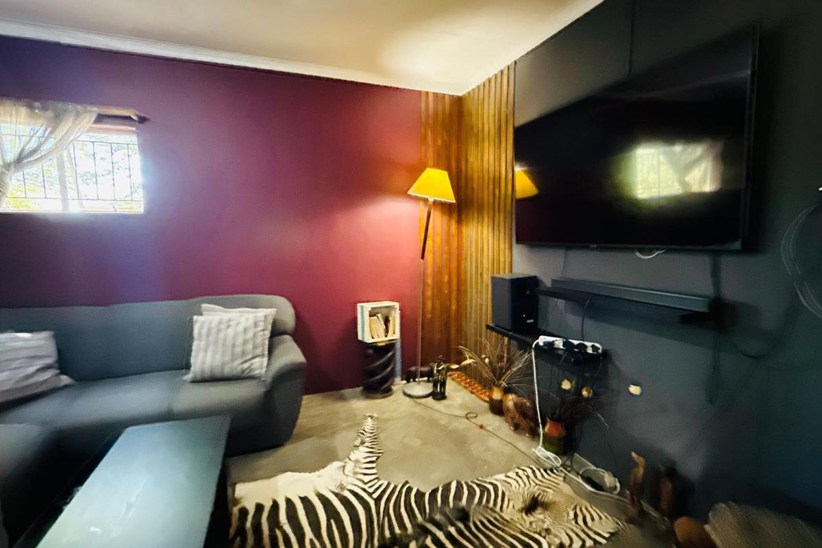 A living room featuring a bold purple accent wall, timber slat paneling, and polished concrete flooring.