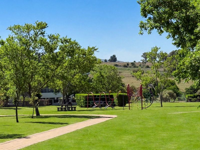 A well-maintained communal garden area featuring expansive green lawns, mature trees, and paved pathways, providing a pleasant outdoor space.
