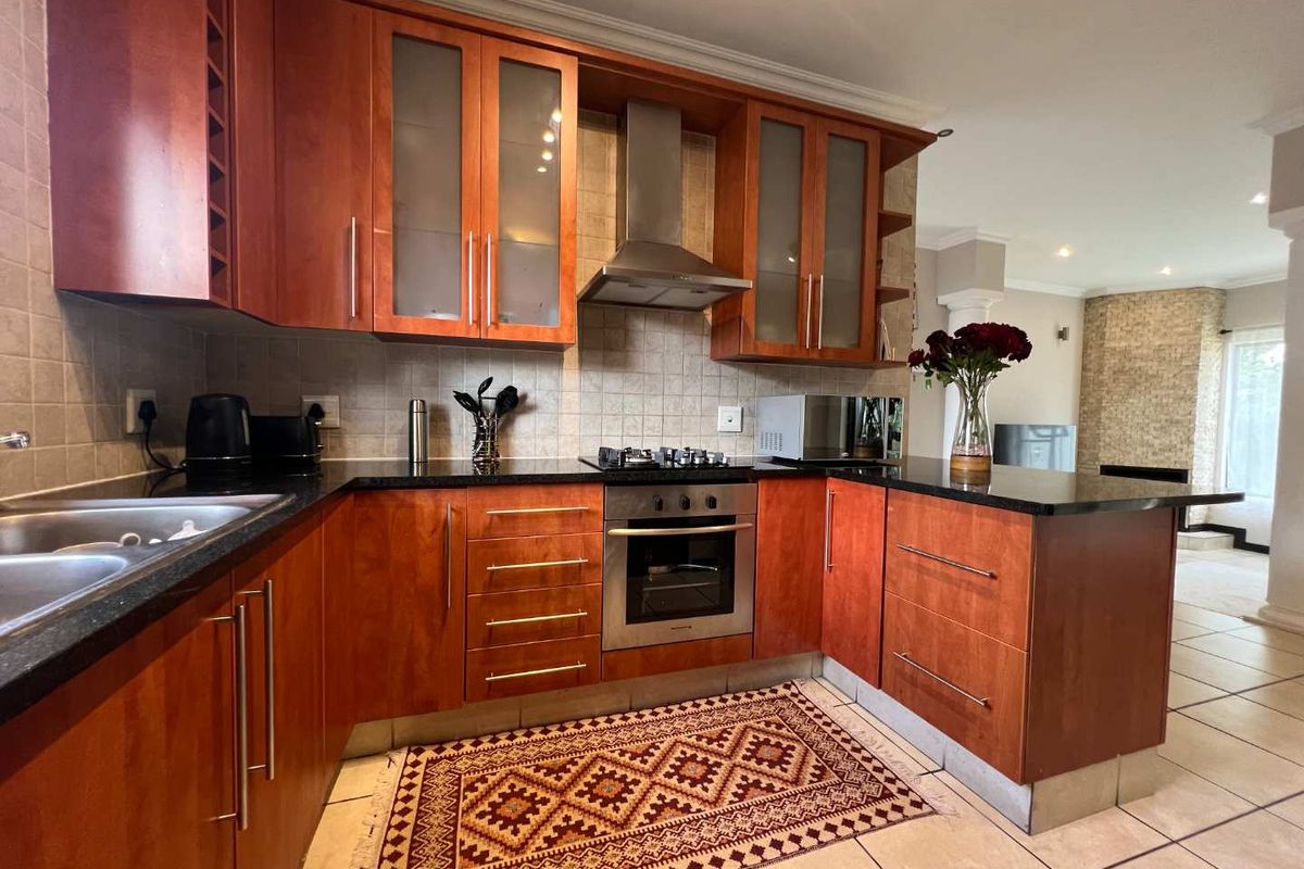 A functional kitchen featuring cherry wood cabinetry, granite countertops, a stainless steel oven, gas hob, and extractor fan, with tiled flooring throughout.