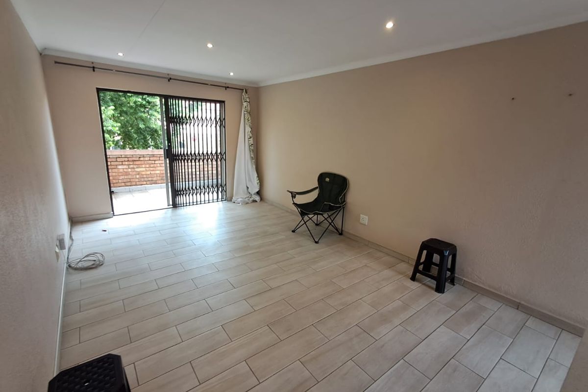 A spacious, light-filled living area featuring modern tiled flooring, recessed ceiling lighting, and a sliding glass door leading to an outdoor balcony.