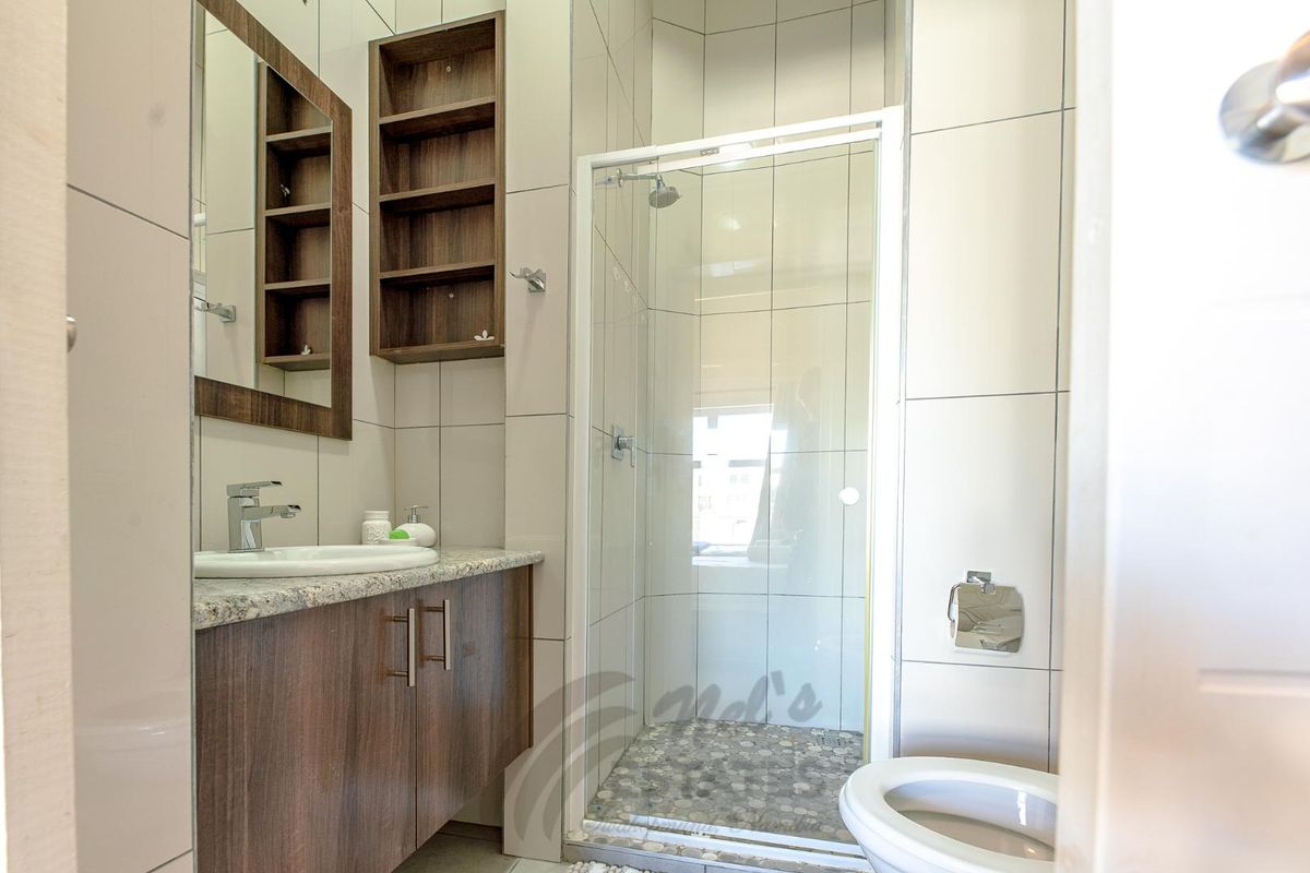 Modern bathroom featuring a glass-enclosed shower with pebble-style flooring, a vanity with granite countertop, and built-in wooden shelving.