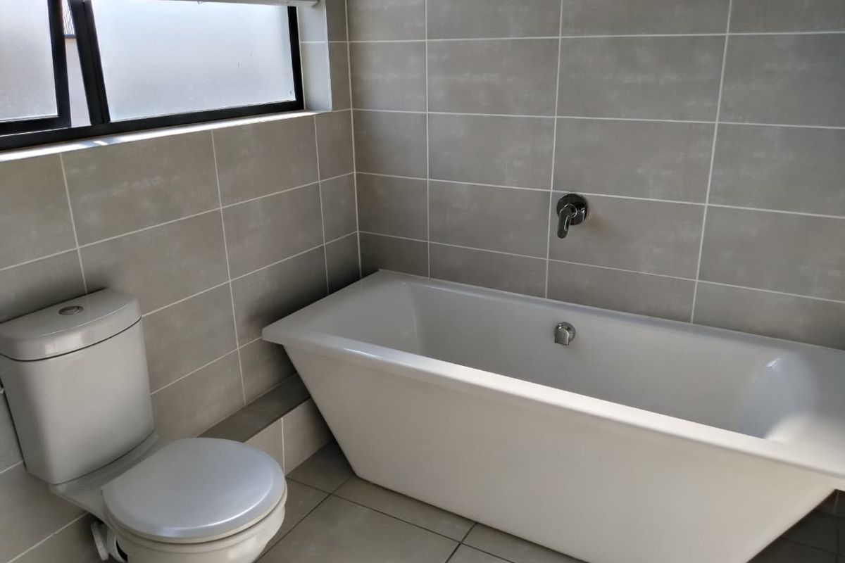 A modern, clean bathroom featuring a sleek freestanding bathtub, wall-mounted faucet, and neutral tiled finishes throughout.