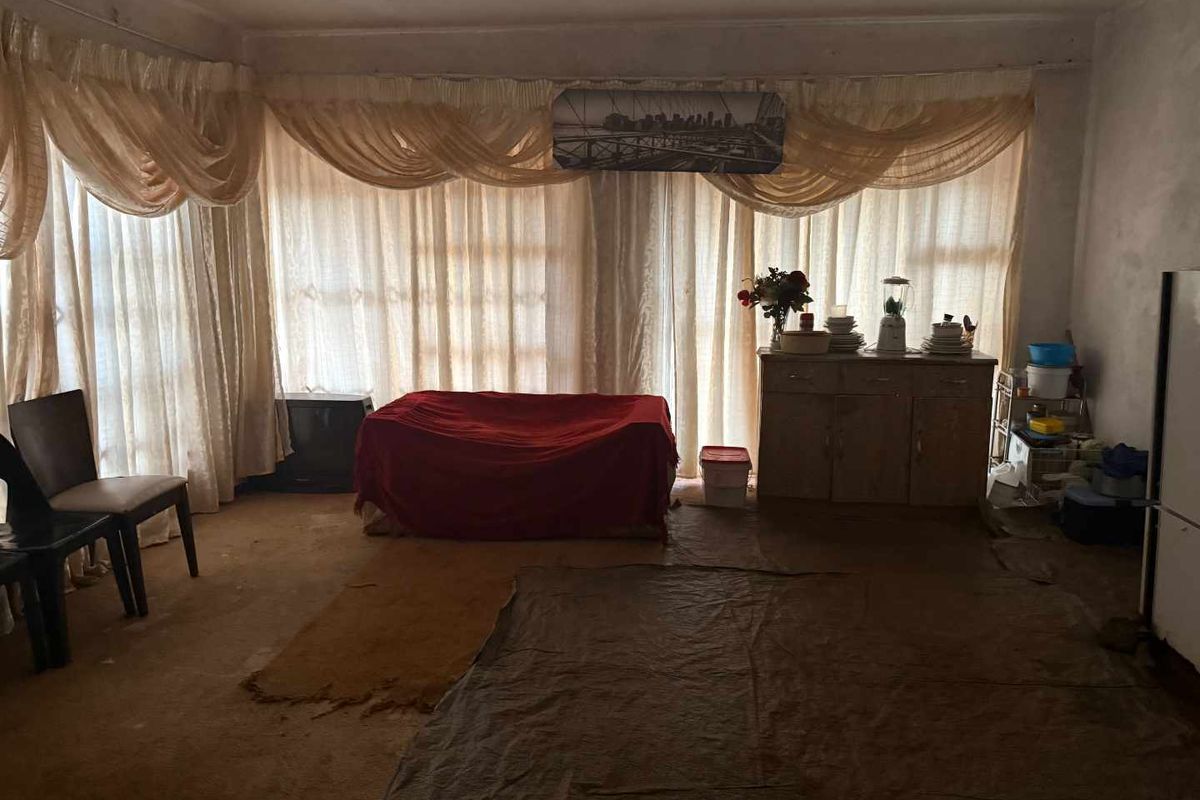A spacious living area featuring large windows with draped curtains and worn flooring, offering a blank canvas for renovation and modernization.