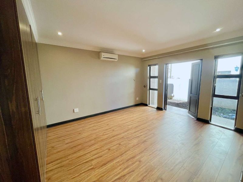 A bright, empty bedroom featuring laminate flooring, built-in cupboards, an air conditioning unit, and direct access to an outdoor area through glass doors.