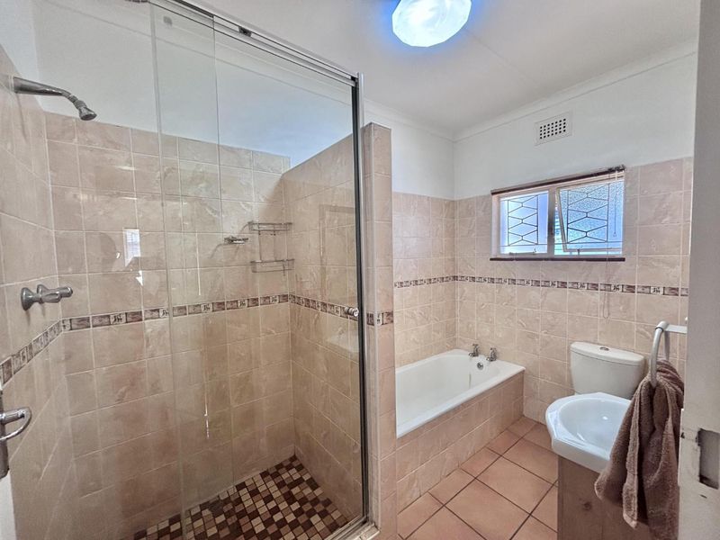 A functional bathroom featuring a glass-enclosed shower, a built-in bathtub, a pedestal basin, and neutral ceramic wall and floor tiles.