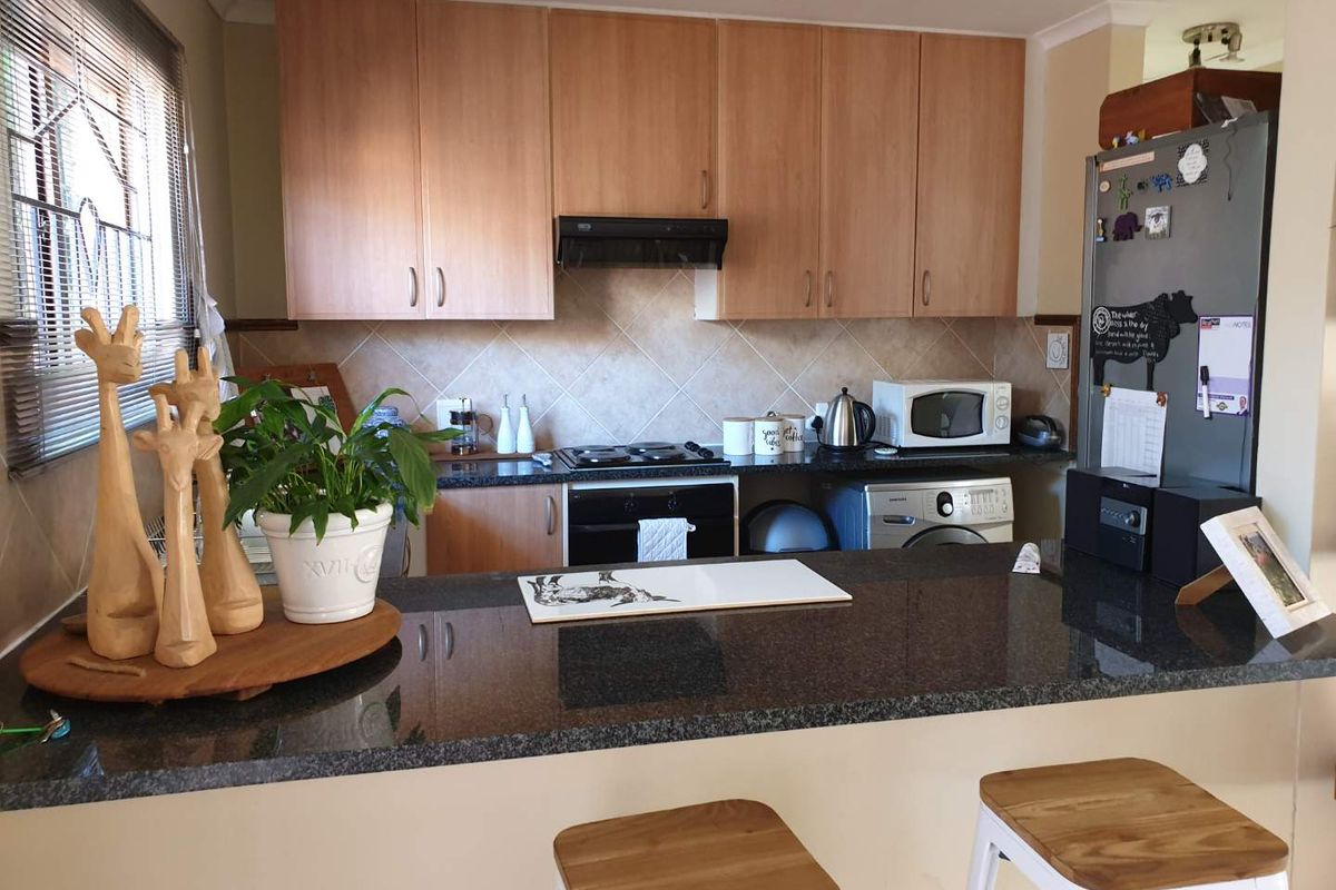 A functional kitchen featuring light wood cabinetry, dark granite countertops, a breakfast bar, and built-in oven with extractor fan.