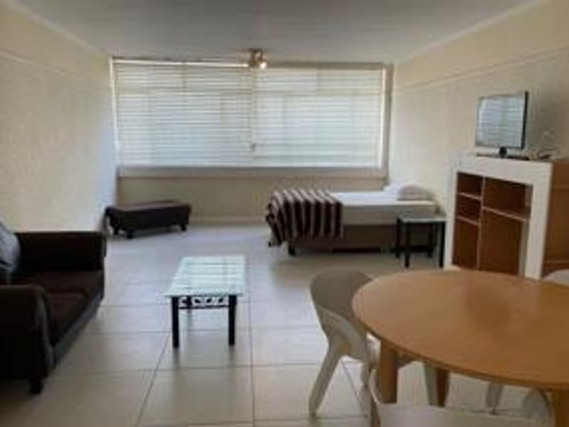 An open-plan living and sleeping area featuring tiled flooring, large windows with venetian blinds, and a functional layout suitable for versatile use.