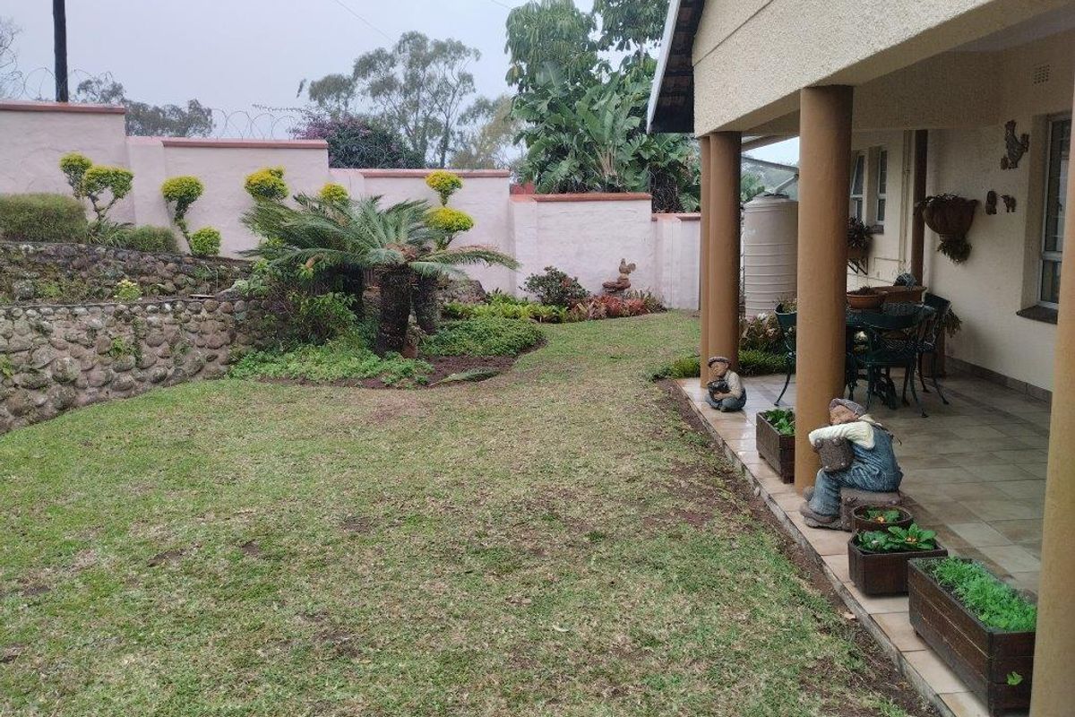 A rear garden area featuring a covered patio with tiled flooring, a stone retaining wall, and a perimeter wall with security fencing.